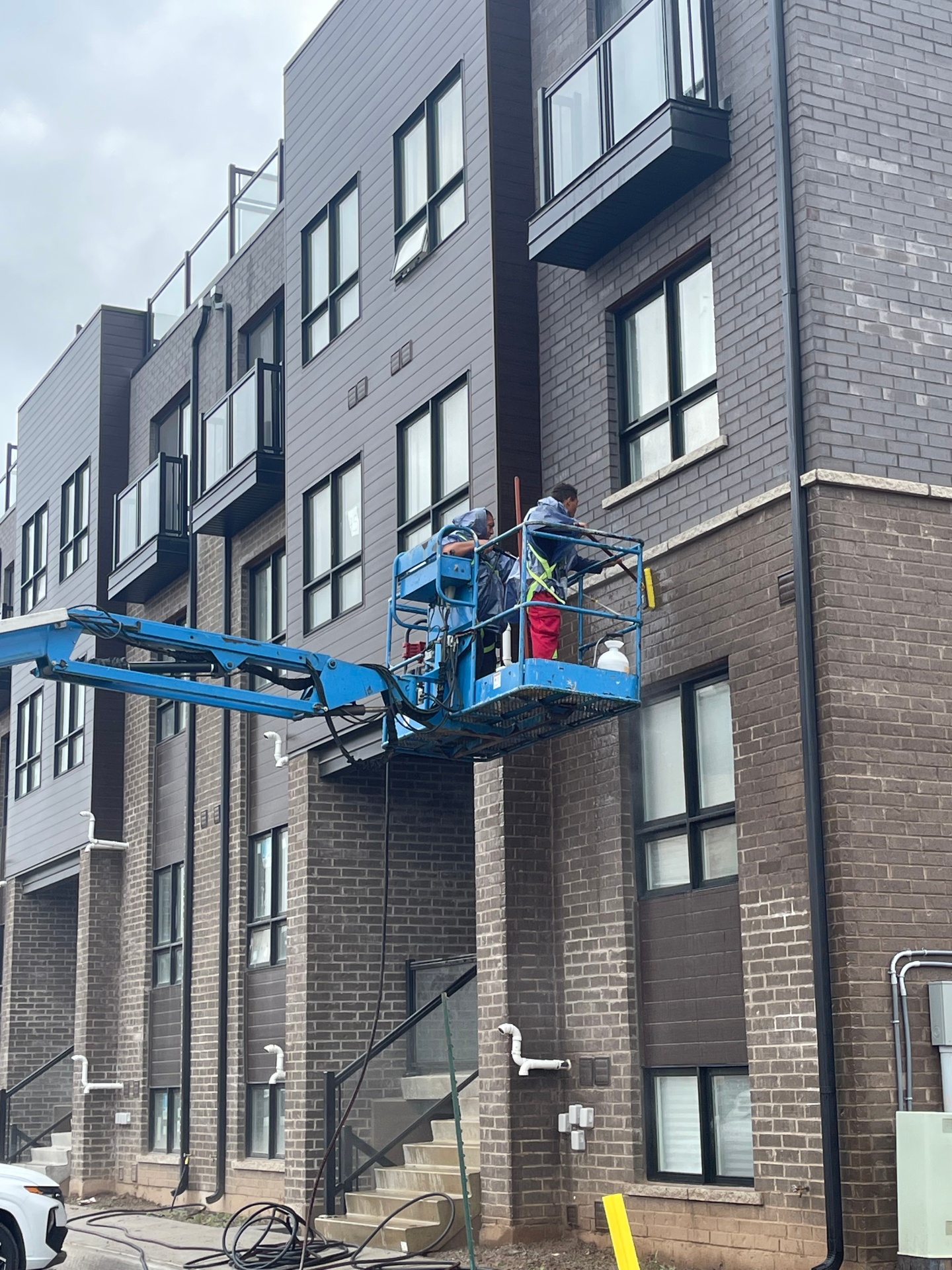 The Brick Doctor crew cleaning a multi-storey brick apartment building from a boom lift in Hamilton