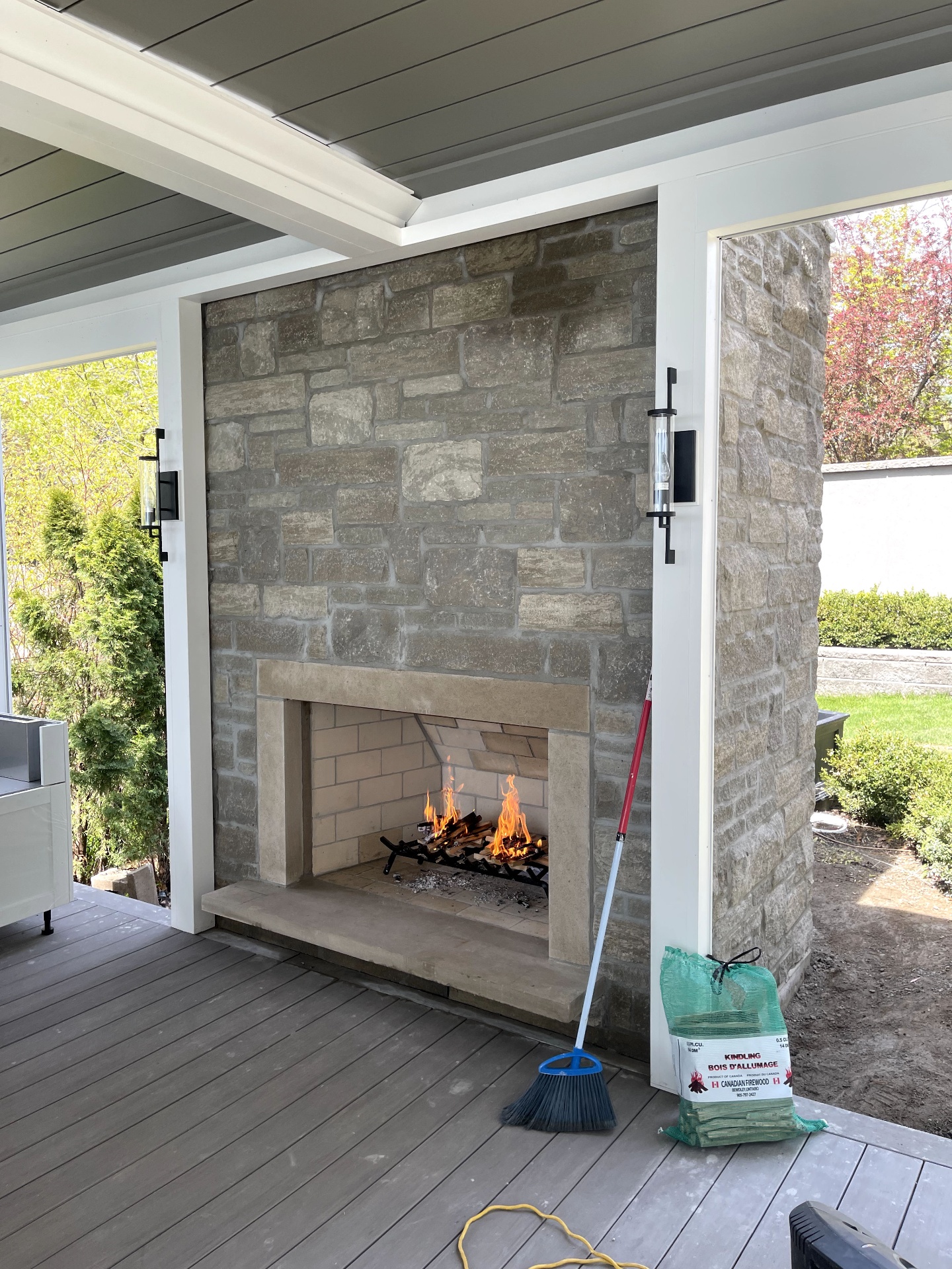 Custom outdoor stone fireplace with cast stone mantel and lit fire on a covered patio
